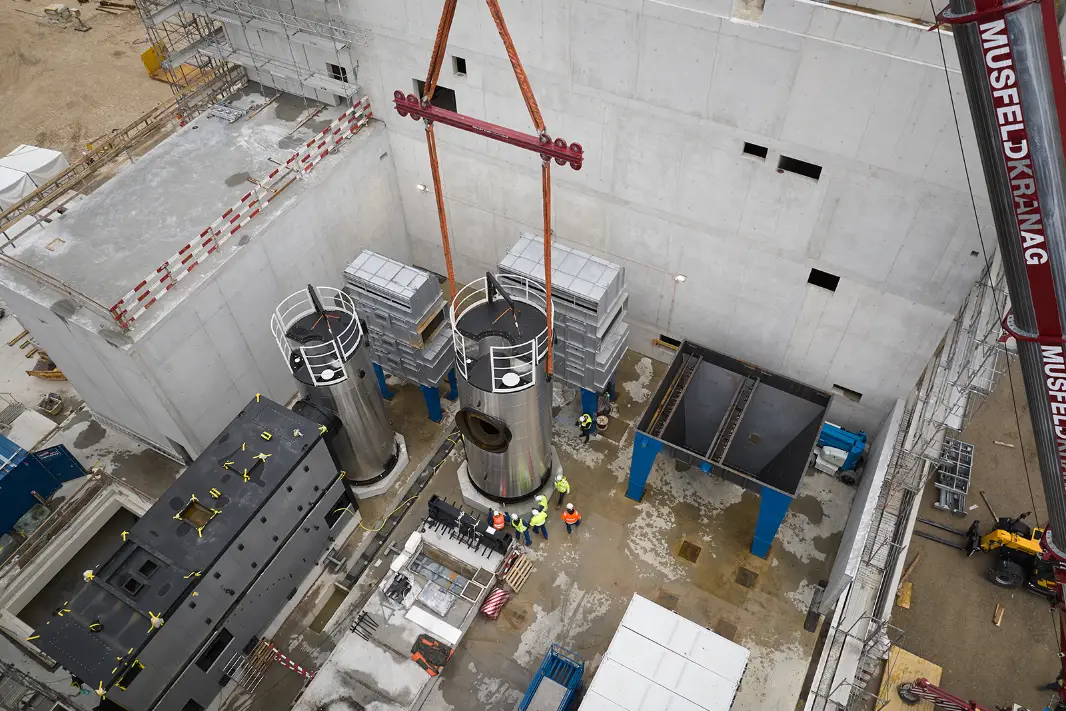 Construction site of the UpTown Basel energy centre. Large cylindrical metal tanks are lifted into position by a crane under the supervision of workers. 