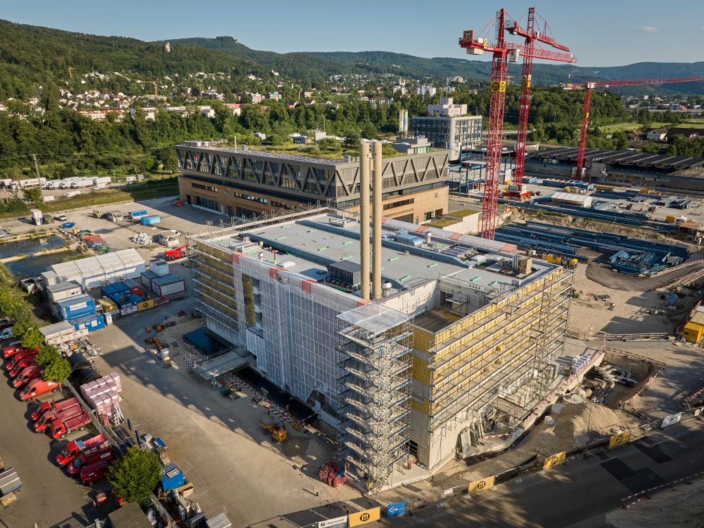Aerial view of the UpTown Basel construction site. The picture shows a large building under construction, surrounded by scaffolding and construction cranes.